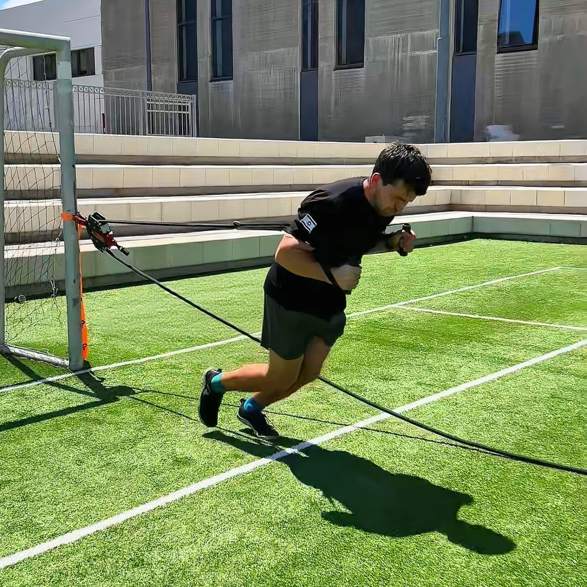 Athlete sprinting on turf against Q-Tail resistance anchored to a goal post