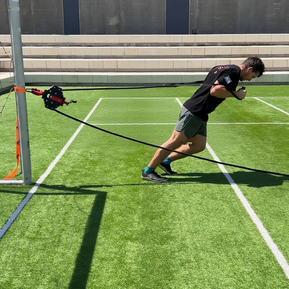 Athlete sprinting on a turf field against Q-Tail resistance anchored to a post
